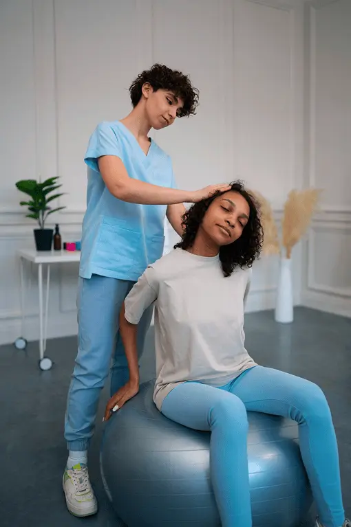 A young woman sitting on a stability ball
            while a physical therapist helps her gently stretch her neck